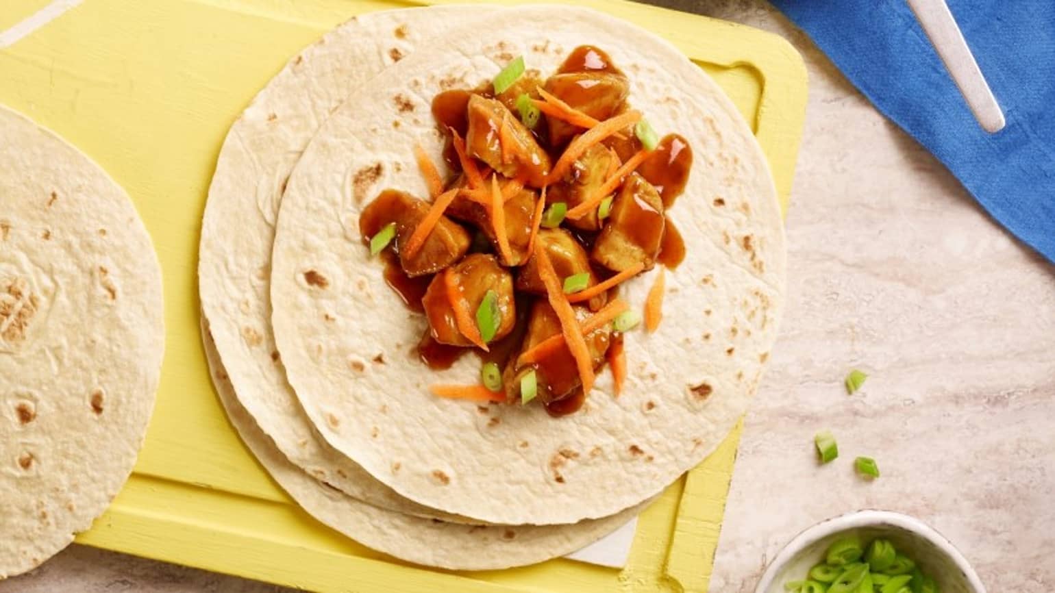 Un plat de fajitas à la saveur teriyaki sur une planche avec du poulet, des carottes et des poireaux